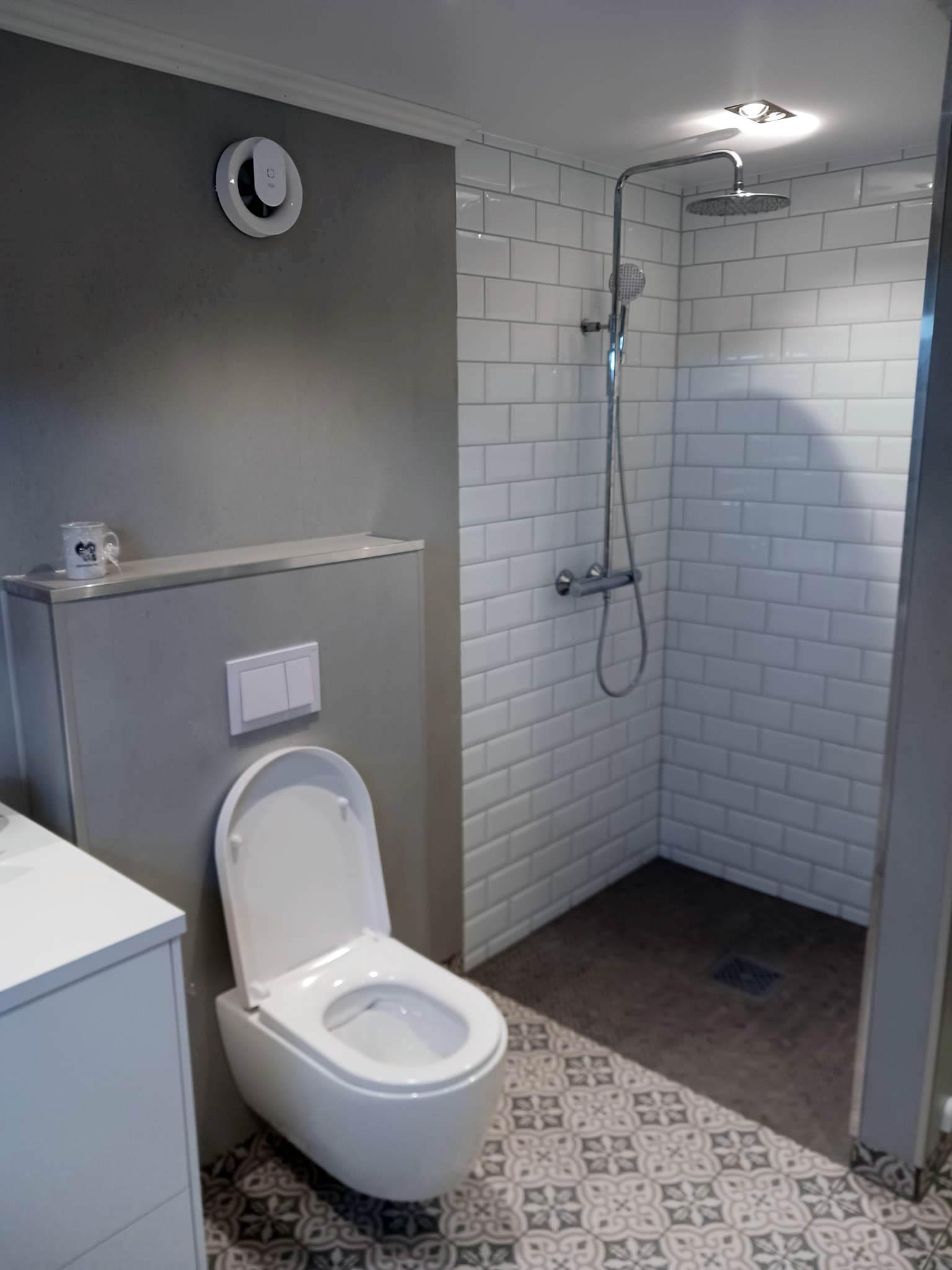 A finished bathroom with white tiles, a wall-hung toilet and a shower