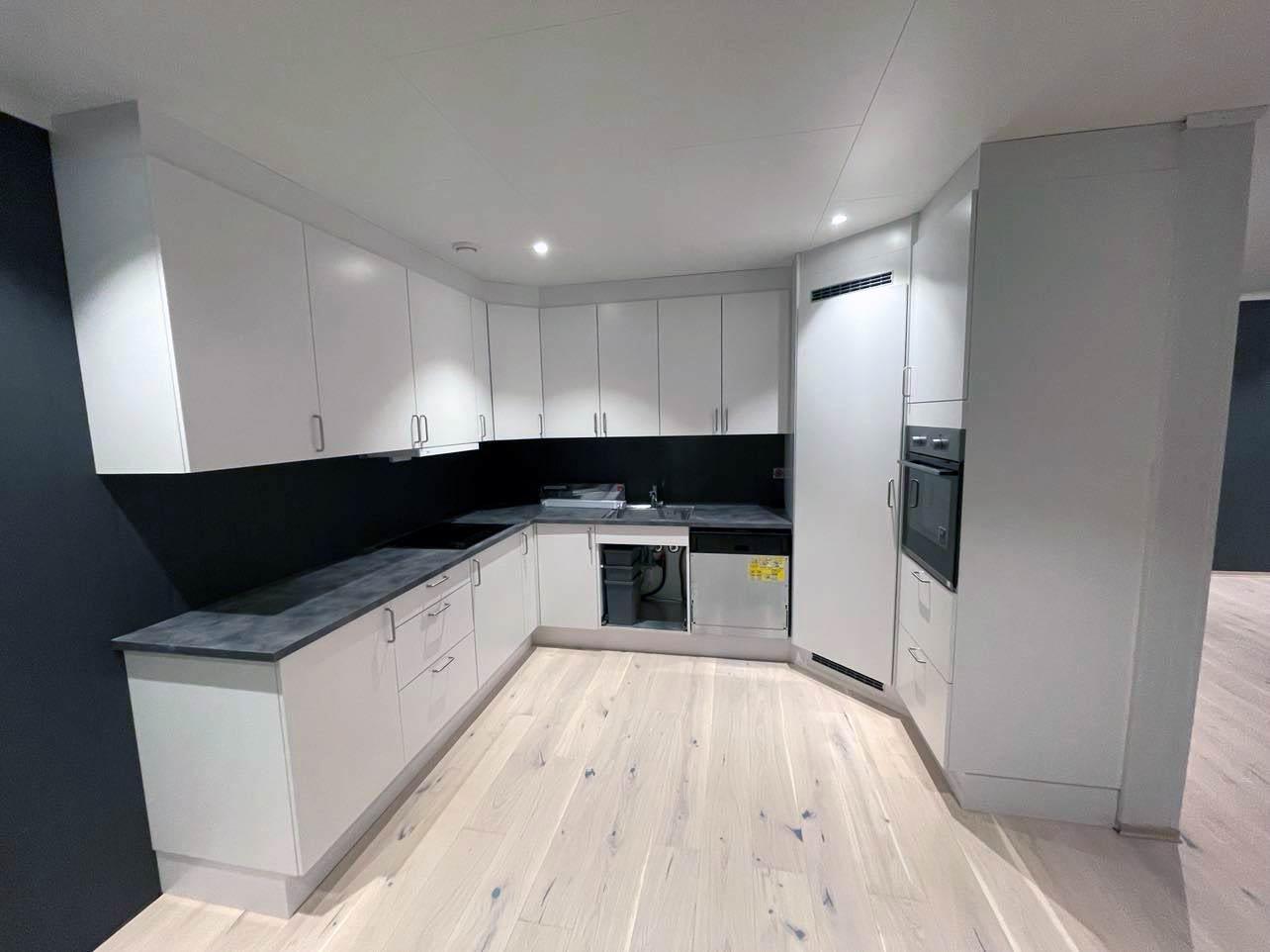A white L-shaped kitchen with a black splashback